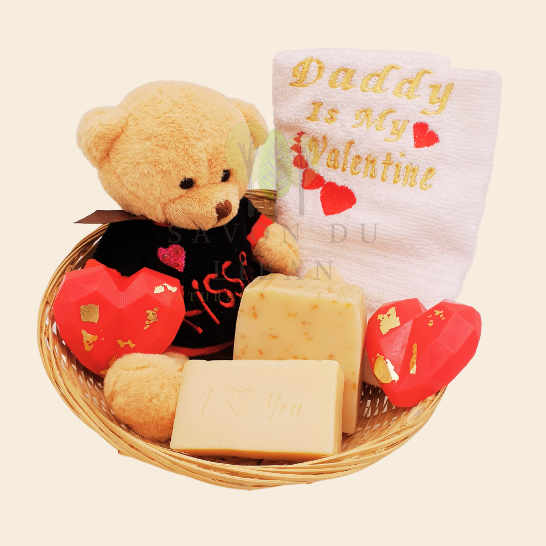 Love Gift Set "Tes Caresses" made of a round straw basket including a Teddy Bear, 2 Heart Soaps, 1 Embroidered Towel, 1 Oat Scrub Soap and 1 Musk Soap stamped with "I ❤️ You".