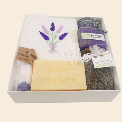 Whispers of Celebration spa set in white box: Sugar Scrub, Bath Salt, Lavender Buds, White Towel with Lavender Embroidery, Musk Soap stamped Joyeux Anniversaire.