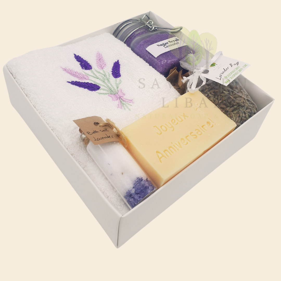 Whispers of Celebration spa set in white box: Sugar Scrub, Bath Salt, Lavender Buds, White Towel with Lavender Embroidery, Musk Soap stamped Joyeux Anniversaire.