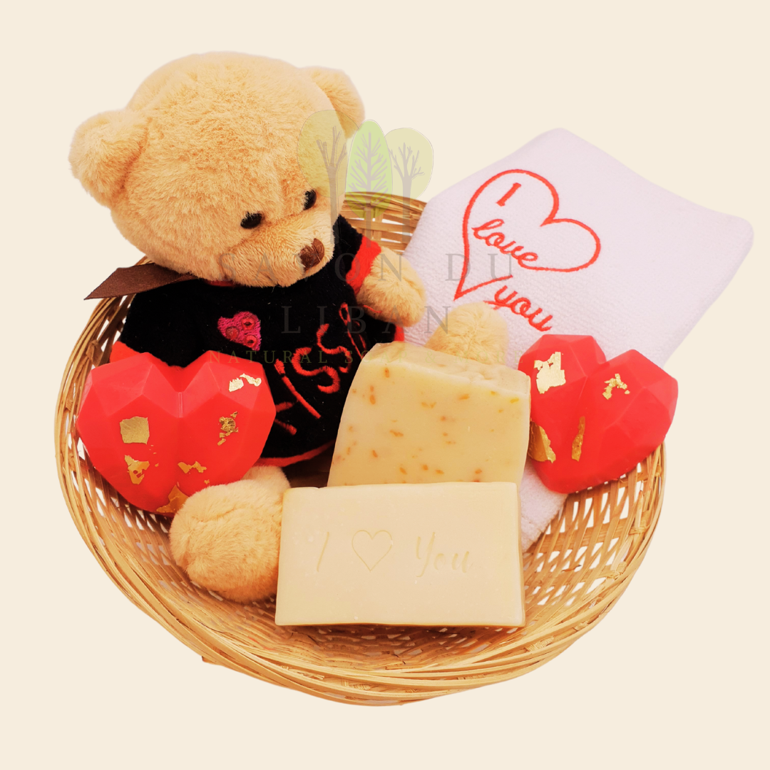 Love Gift Set "Tes Caresses" made of a round straw basket including a Teddy Bear, 2 Heart Soaps, 1 Embroidered Towel, 1 Oat Scrub Soap and 1 Musk Soap stamped with "I ❤️ You".